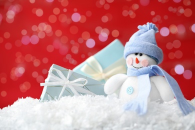 Photo of Snowman toy and Christmas gift boxes on snow against blurred festive lights