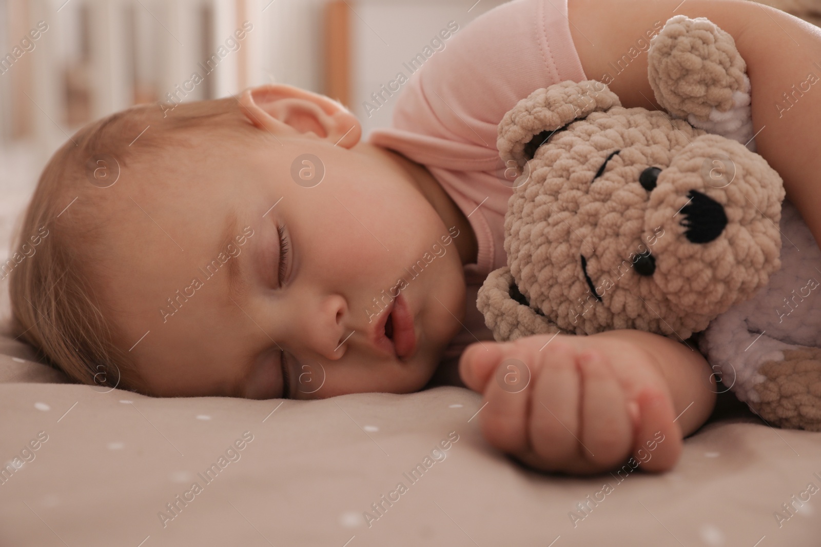 Photo of Adorable little baby with toy bear sleeping on bed at home, closeup