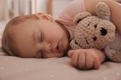 Photo of Adorable little baby with toy bear sleeping on bed at home, closeup