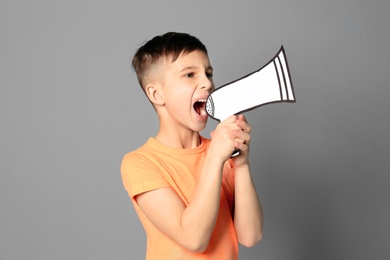 Cute little boy with paper megaphone on grey background