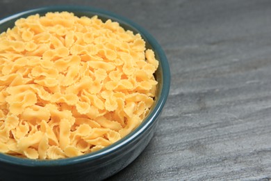 Photo of Raw farfalline pasta in bowl on grey table, closeup. Space for text