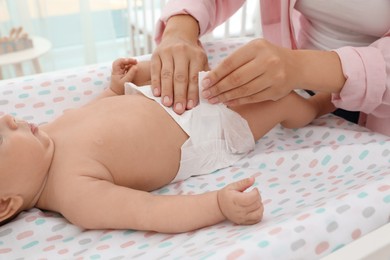 Photo of Mother changing her baby's diaper on table at home, closeup