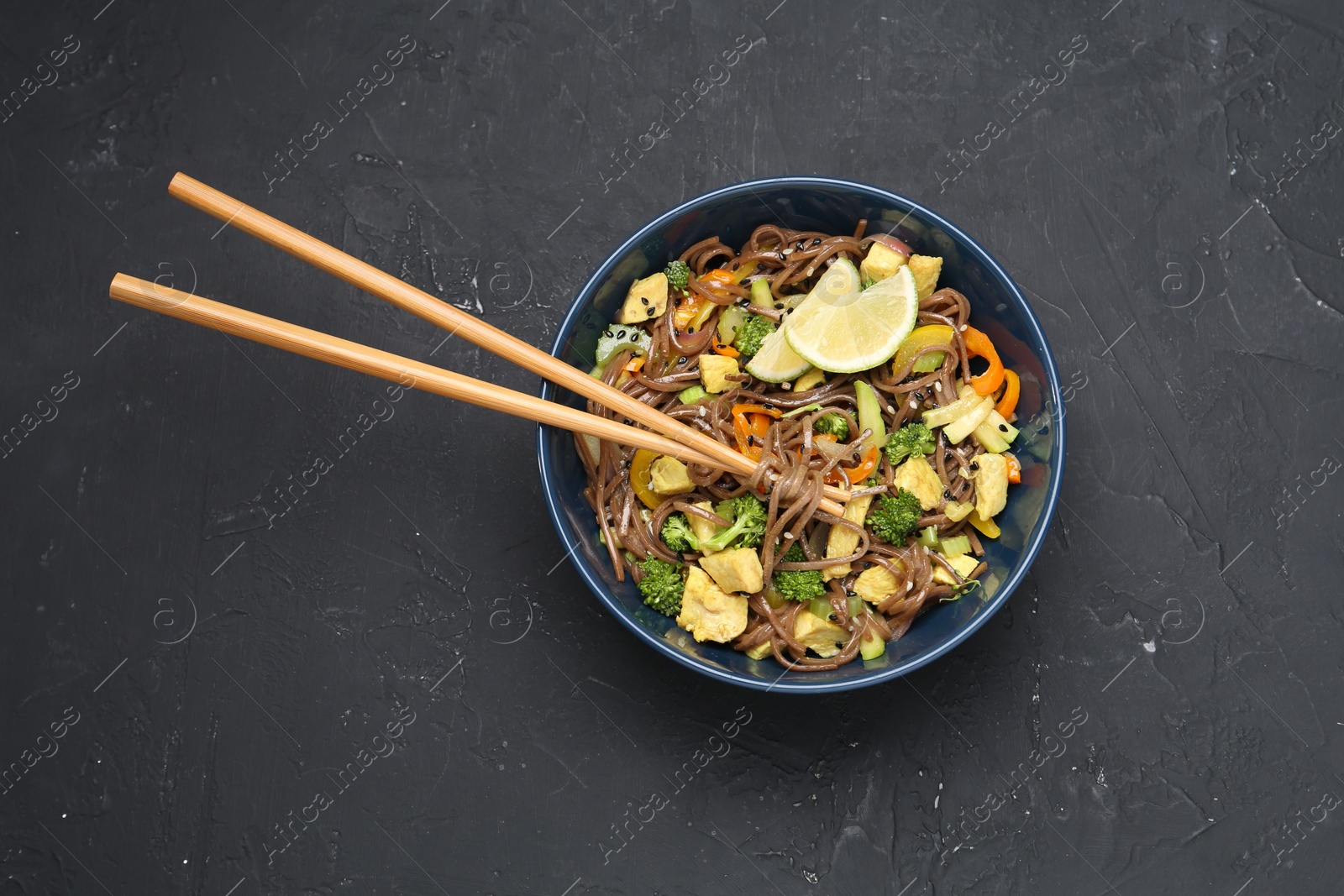 Photo of Stir-fry. Delicious cooked noodles with chicken and vegetables in bowl served on gray textured table, top view