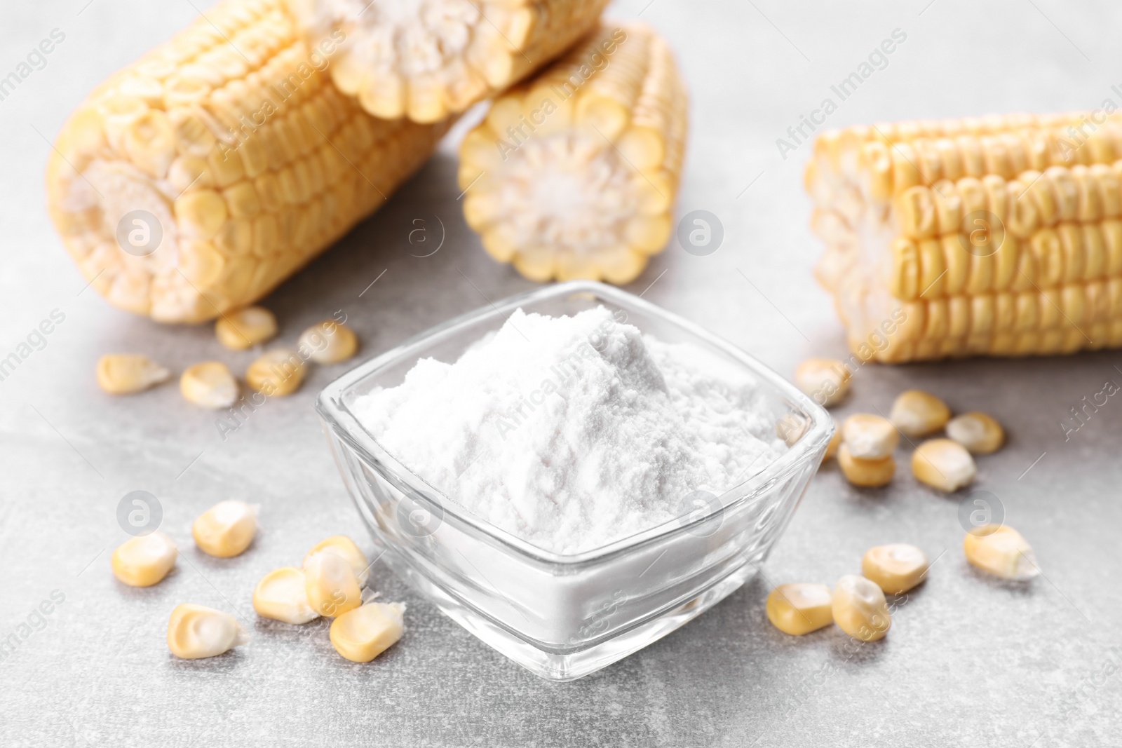Photo of Bowl with corn starch and kernels on light grey table, closeup