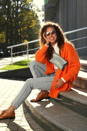 Photo of Beautiful African American woman with stylish waist bag on stairs outdoors