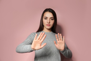 Woman showing STOP gesture in sign language on color background