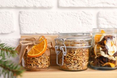 Photo of Jars of dried orange zest seasoning on wooden shelf near white brick wall