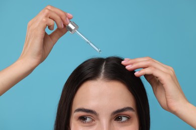 Photo of Woman applying hair serum on light blue background, closeup. Cosmetic product