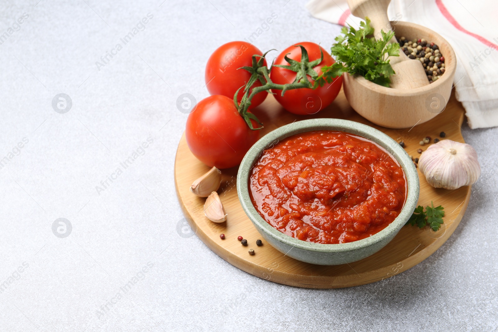 Photo of Homemade tomato sauce in bowl and fresh ingredients on light grey table. Space for text