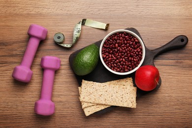 Healthy diet. Measuring tape, dumbbells and products on wooden table, flat lay