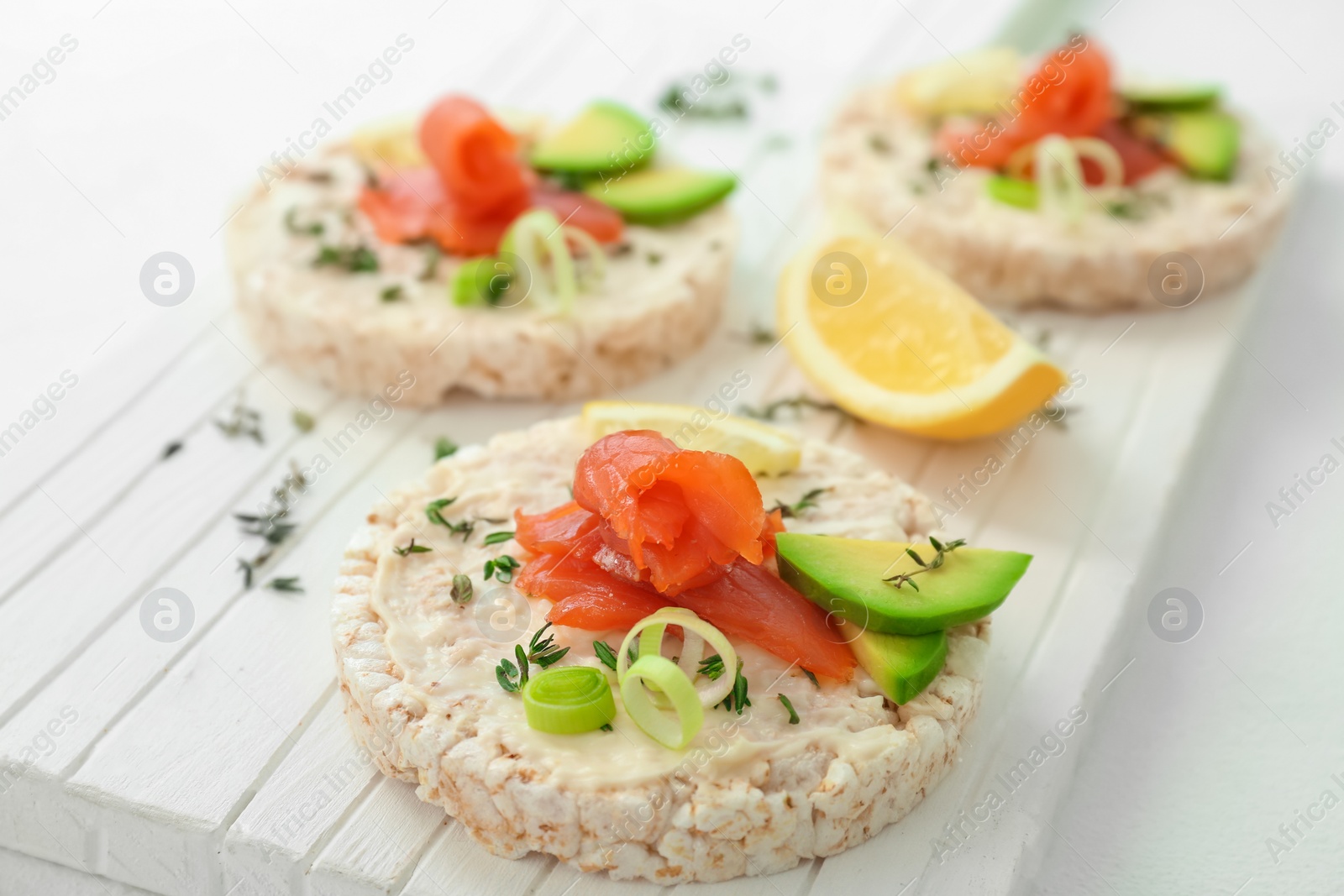 Photo of Crispbreads with fresh sliced salmon fillet and avocado on wooden board, closeup