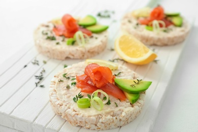 Photo of Crispbreads with fresh sliced salmon fillet and avocado on wooden board, closeup