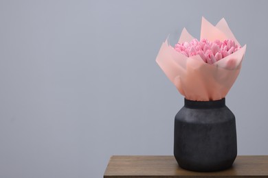 Photo of Bouquet of beautiful pink tulips in vase on wooden table against light grey background, space for text