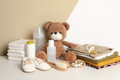 Baby clothes, toy bear and accessories on white table