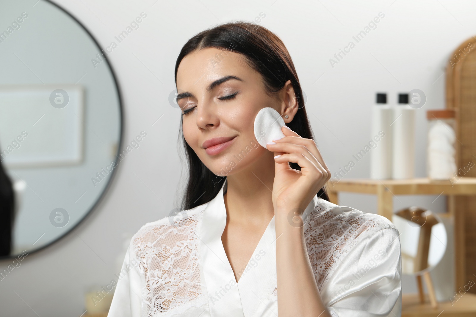 Photo of Young woman using cotton pad with micellar water indoors