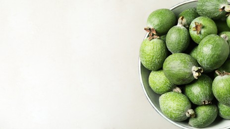 Image of Fresh green feijoa fruits in bowl on light grey table, top view with space for text. Banner design