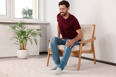 Photo of Man suffering from leg pain on soft armchair at home