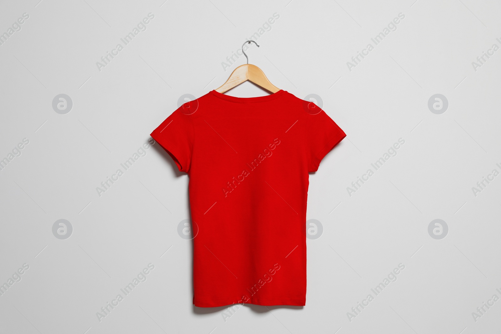 Photo of Hanger with red t-shirt on light wall. Mockup for design