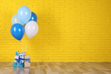 Gift boxes and balloons near yellow brick wall. Space for text