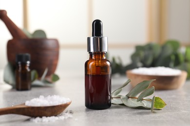 Photo of Aromatherapy. Bottle of essential oil, sea salt and eucalyptus leaves on grey table