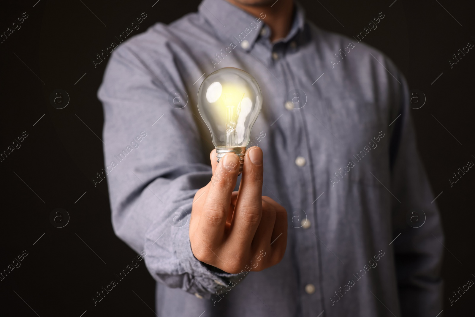 Photo of Glow up your ideas. Closeup view of man holding light bulb on black background