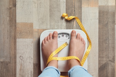 Photo of Woman with tied legs measuring her weight using scales on floor. Healthy diet