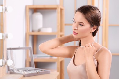 Photo of Young woman trying on elegant pearl necklace at dressing table indoors, space for text