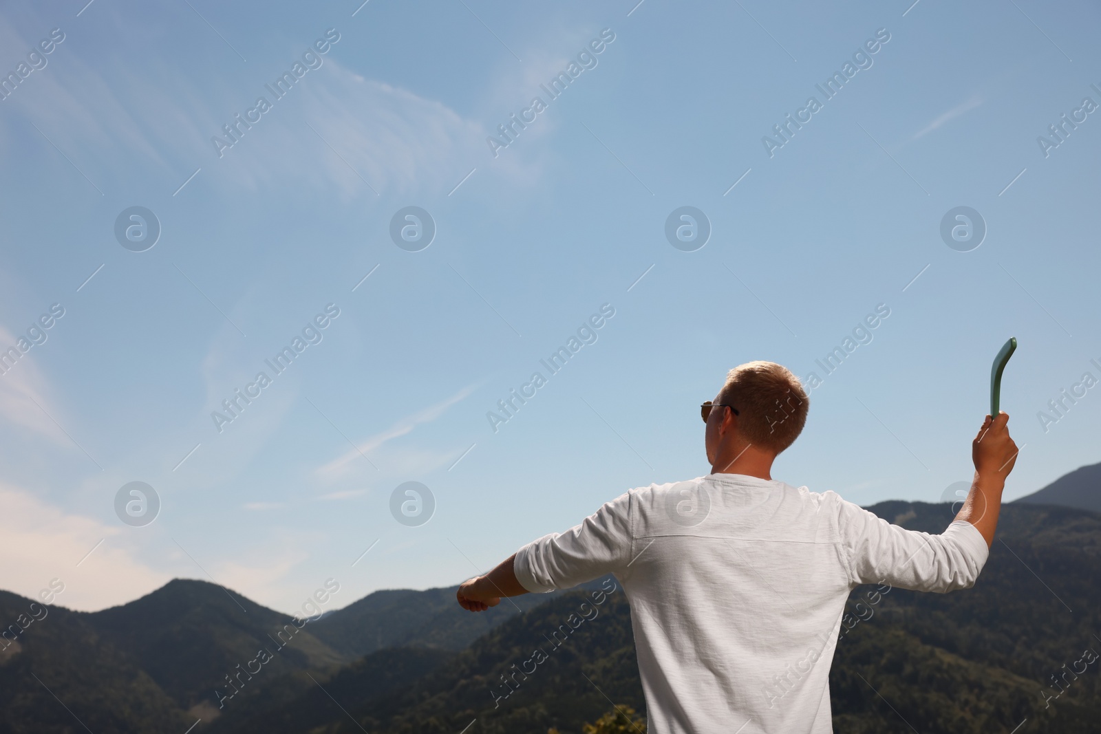 Photo of Man throwing boomerang in mountains on sunny day, back view. Space for text