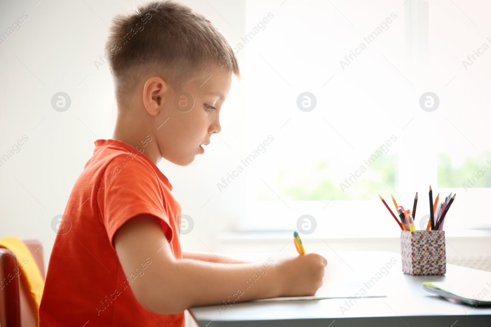 Photo of Cute little child doing assignment at desk in classroom. Elementary school