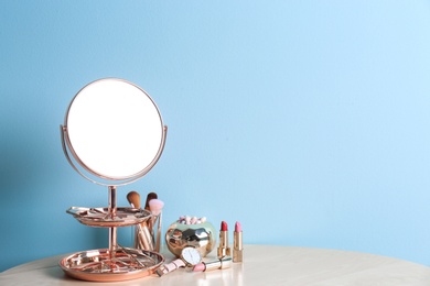 Photo of Modern mirror with makeup products and accessories on table near color wall