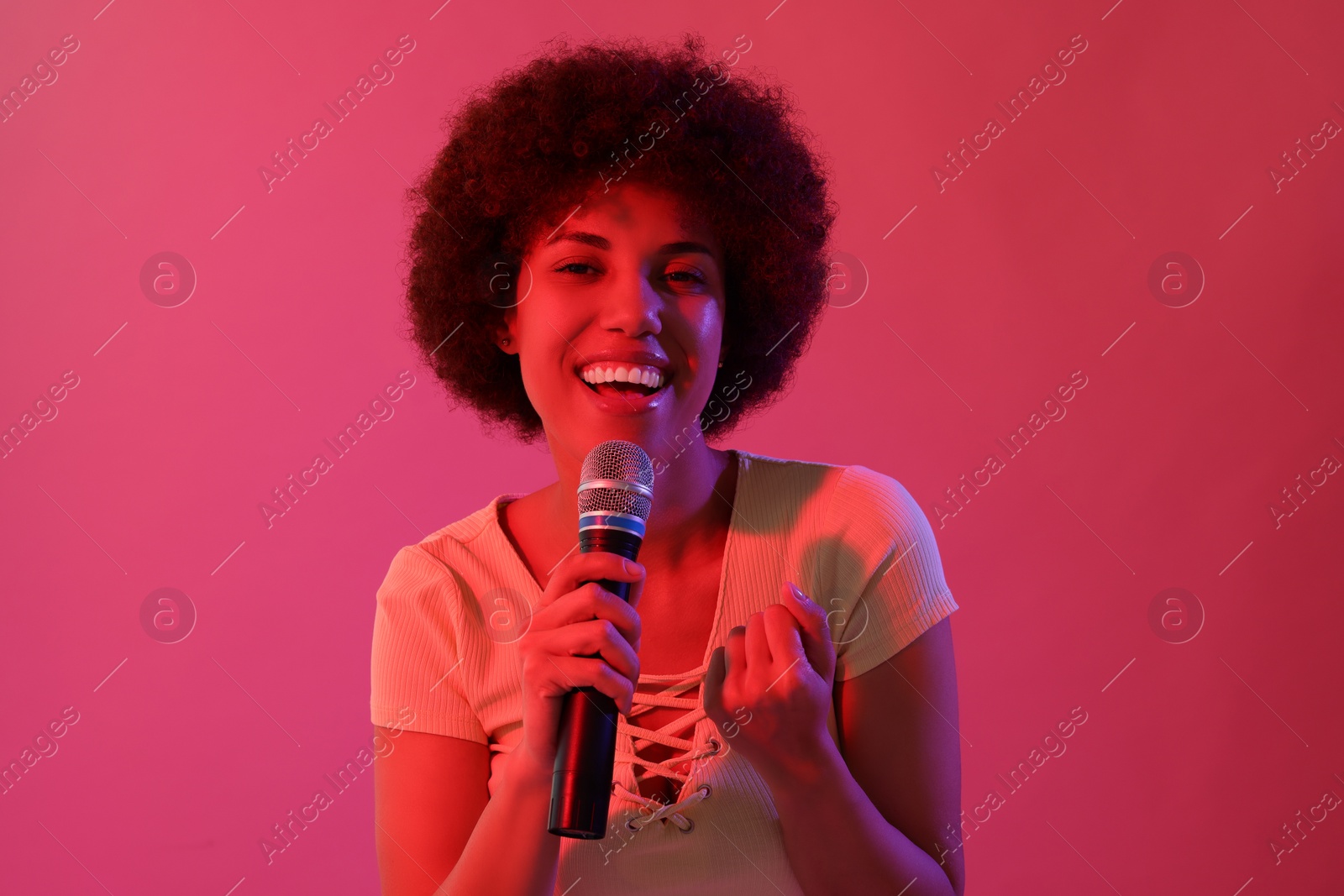 Photo of Curly young woman with microphone singing on pink background. Color tone effect