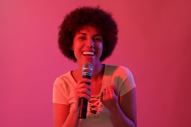 Curly young woman with microphone singing on pink background. Color tone effect