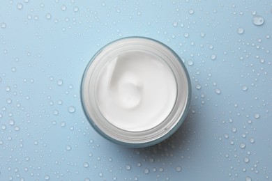 Photo of Jar of face cream on light blue surface covered with water drops, top view
