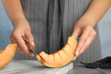 Young woman cutting cantaloupe melon slice at table, closeup