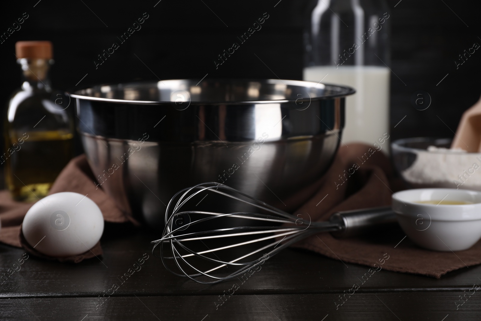 Photo of Making dough. Metal whisk and ingredients on dark wooden table, closeup