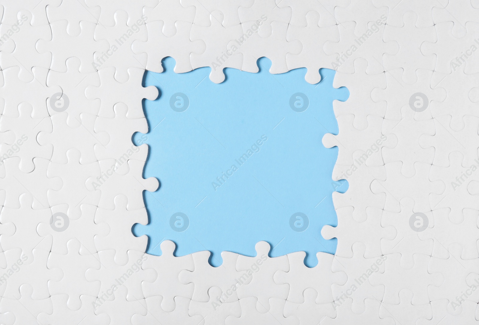 Photo of Frame made with white puzzle pieces on light blue background, top view. Space for text