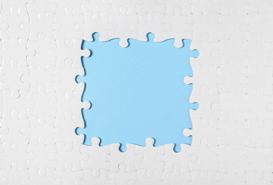 Photo of Frame made with white puzzle pieces on light blue background, top view. Space for text