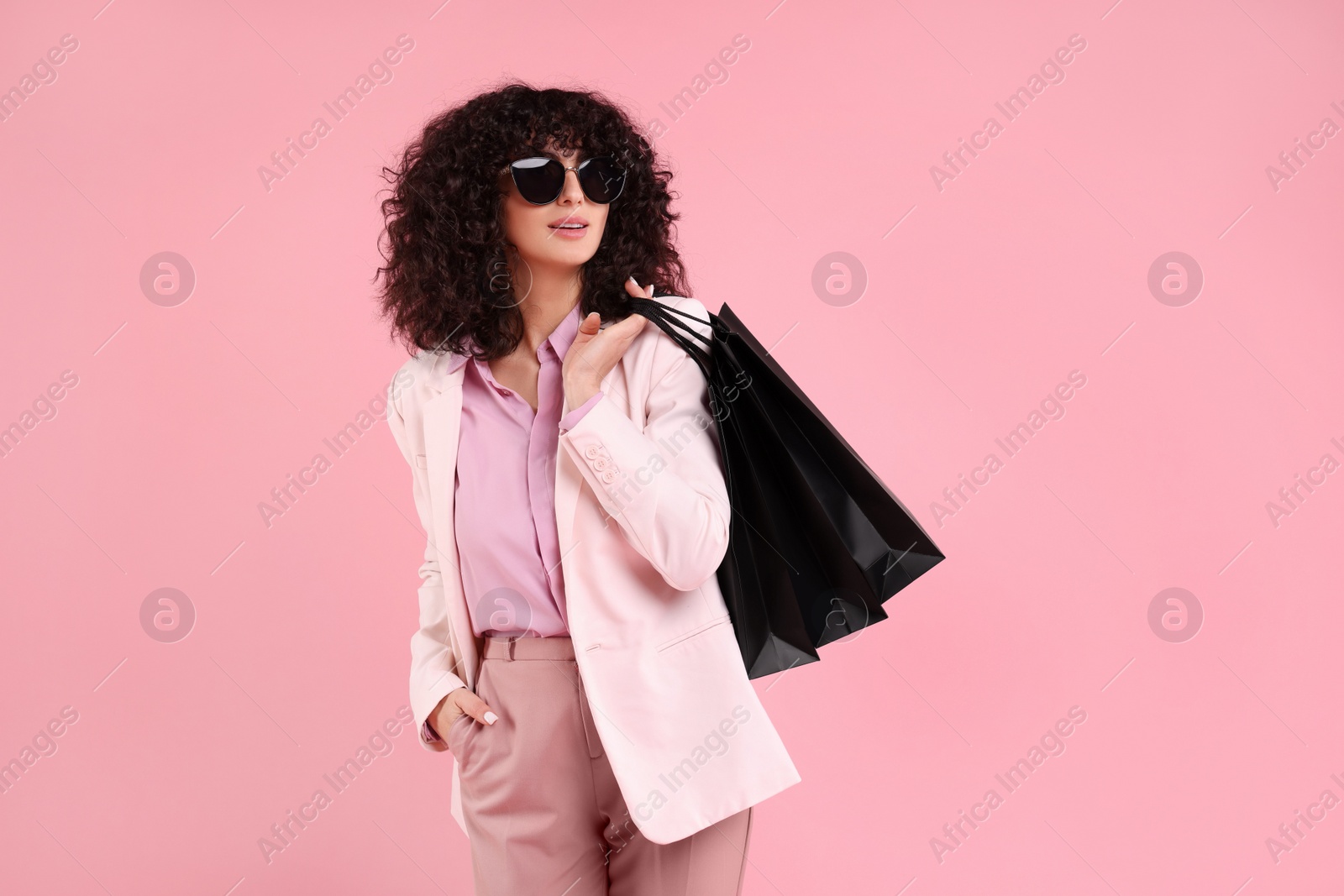 Photo of Happy young woman with shopping bags and stylish sunglasses on pink background. Space for text