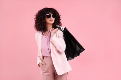 Happy young woman with shopping bags and stylish sunglasses on pink background. Space for text