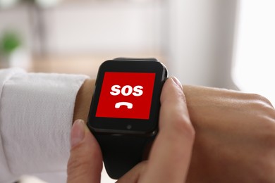 Woman using SOS function on smartwatch indoors, closeup