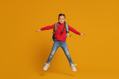 Happy schoolgirl with backpack jumping on orange background