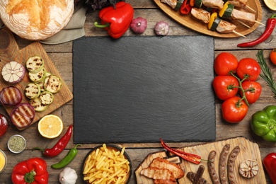 Flat lay composition with barbecued meat and vegetables on wooden table. Space for text