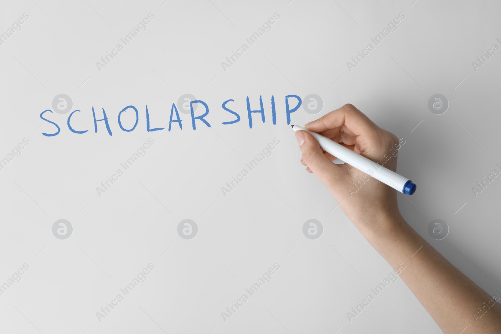 Image of Woman writing word SCHOLARSHIP on white paper, closeup