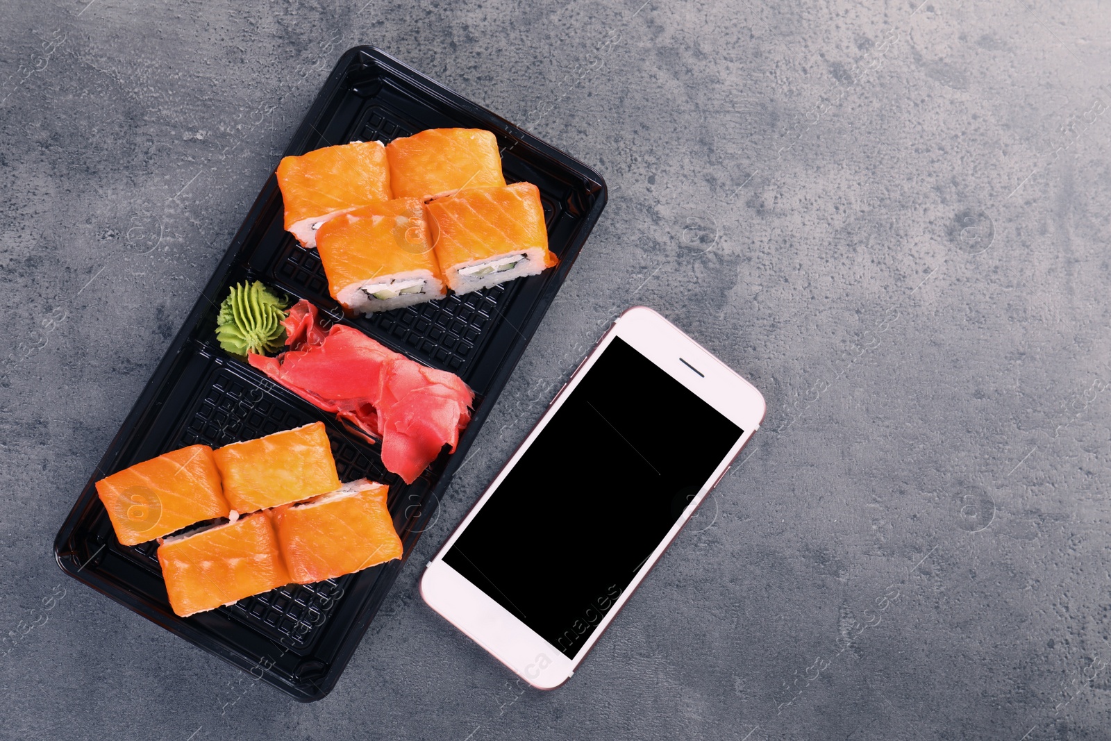 Photo of Tasty sushi rolls and smartphone with space for text on grey table, top view. Food delivery