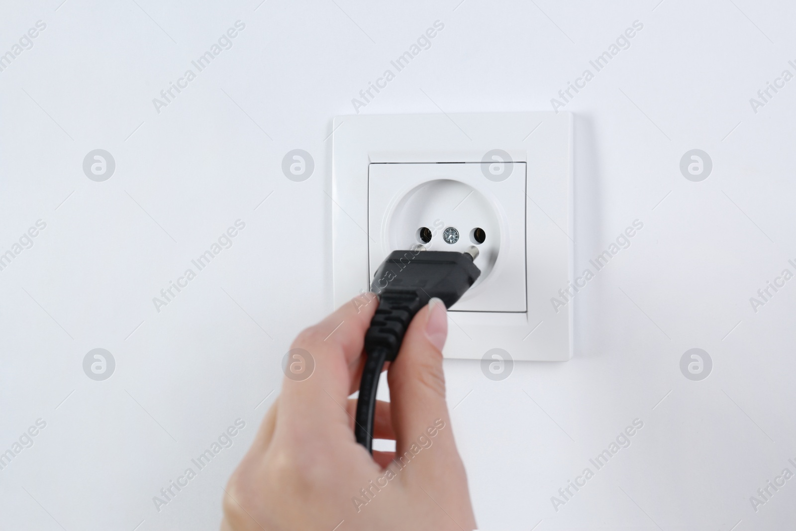 Photo of Woman putting plug into power socket on white background, closeup. Electrician's equipment