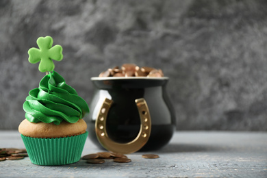 Decorated cupcake and pot with gold coins on grey wooden table, space for text. St. Patrick's Day celebration