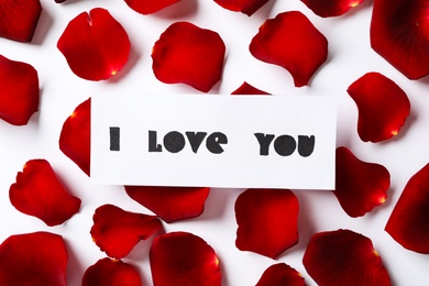 Card with text I Love You and red rose petals on white background, top view