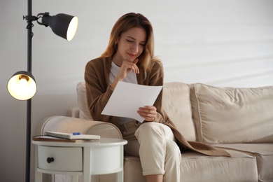 Photo of Happy woman reading letter on sofa at home