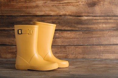 Photo of Pair of yellow rubber boots on wooden surface. Space for text