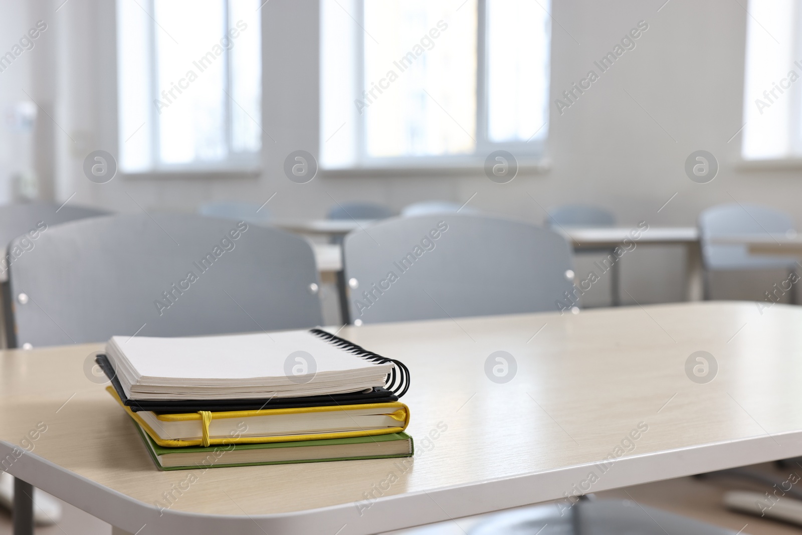 Photo of Stack of notebooks on wooden desk in empty classroom. Space for text